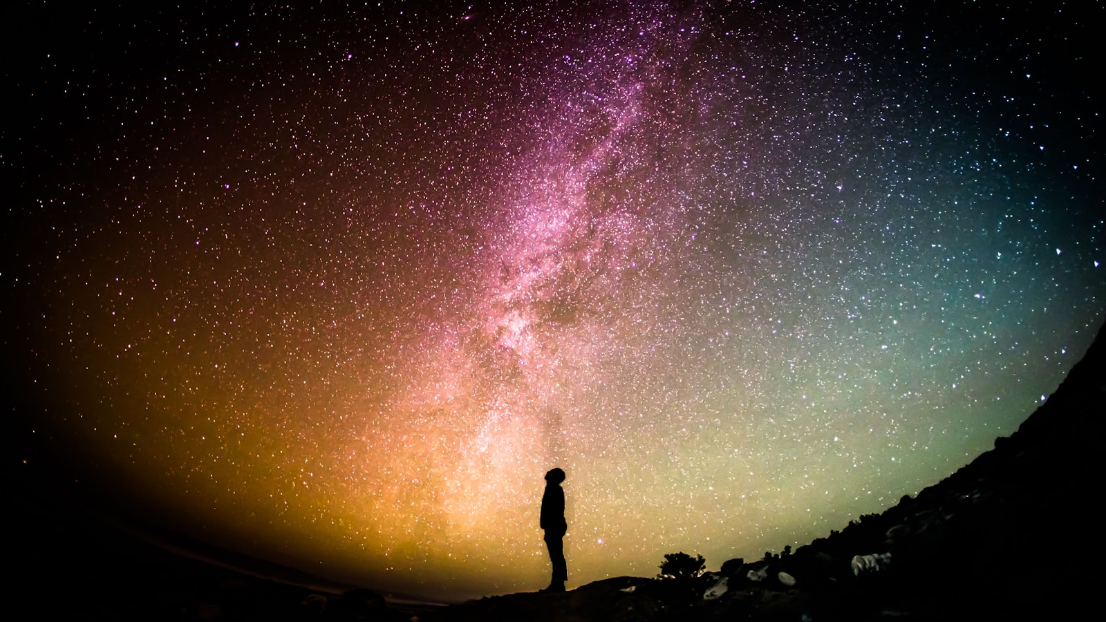 A person standing under a vast star-filled night sky on a dark hillside