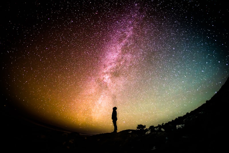 A person standing under a vast star-filled night sky on a dark hillside